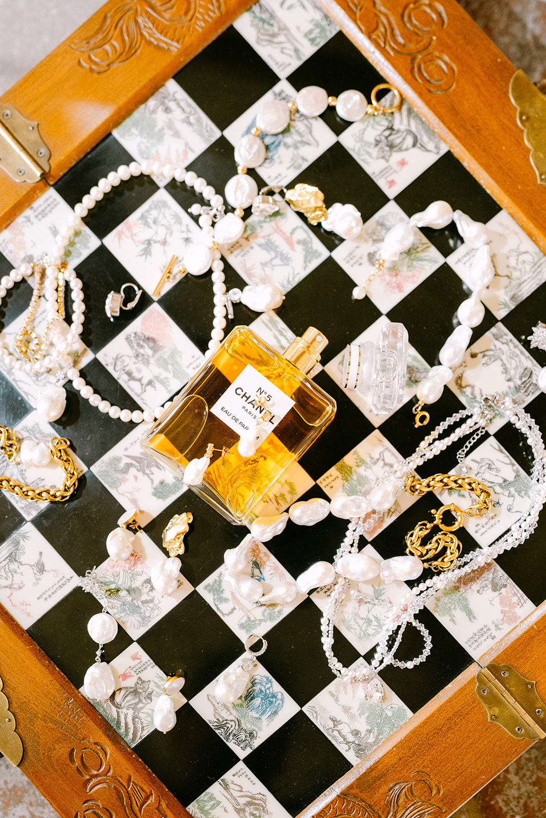 Bridal jewelry, pearl accessories and perfume arranged on a chessboard for a wedding at Château du Boulay-Morin in Normandy